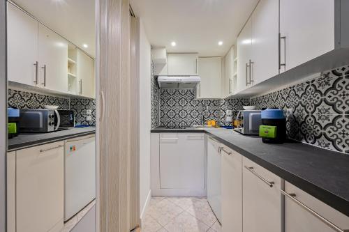 une cuisine avec des armoires blanches et du carrelage noir et blanc dans l'établissement Le Saisonnier - Charme & Confort - Porte de Paris, à Saint-Ouen