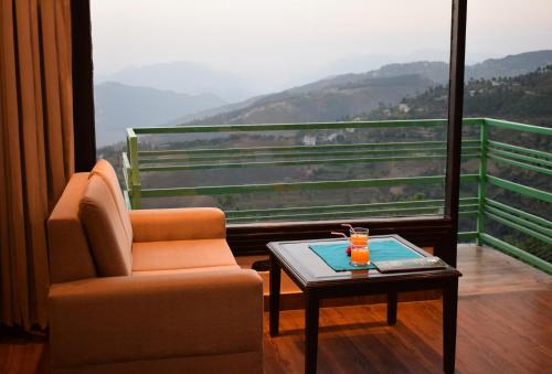 Habitación con silla, mesa y vistas. en Nature Mountain Valley View Resort -- A Four Star Luxury Resort en Shimla