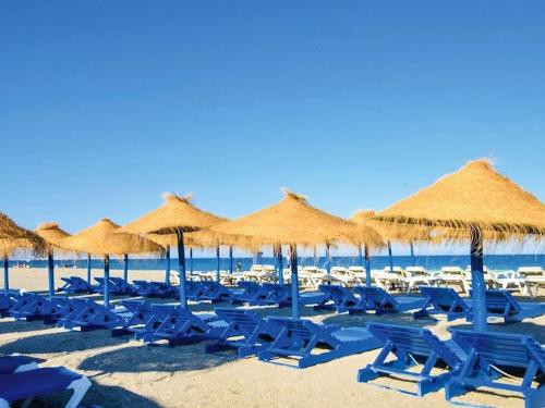 Beautiful holiday home in Roquetas de Mar by the sea في روكويتاس دي مار: شاطئ به كراسي زرقاء ومظلات القش