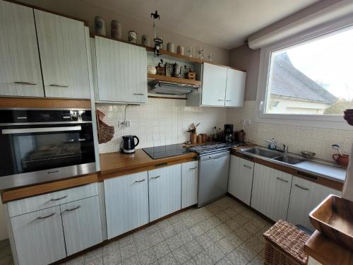 une cuisine avec des placards blancs et une grande fenêtre dans l'établissement Paisible oasis ! Grande maison familiale, à Plouescat