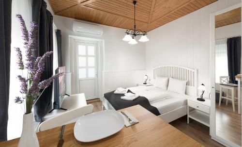 a white bedroom with a bed and a desk and a table at Provence Apartmanok in Visegrád
