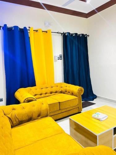 a living room with yellow couches and blue curtains at Guest Bakhita in Abomey-Calavi