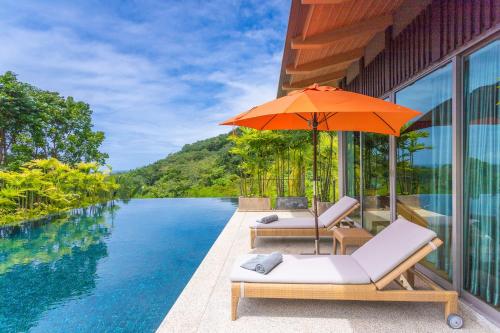 a pool with two chairs and an umbrella next to a swimming pool at Teetara Villa Patong in Patong Beach