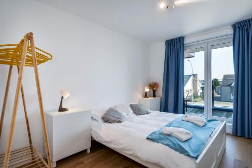 a bedroom with a bed with blue curtains and a window at Flat White - Luxe app aan zee met terras & parking in De Haan