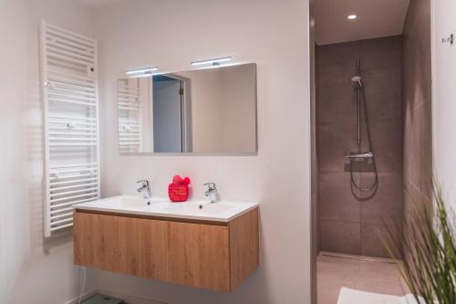 a bathroom with a sink and a shower with a mirror at Flat White - Luxe app aan zee met terras & parking in De Haan