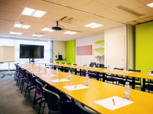 パリにあるイビス パリ ベルシー ビレッジのテーブルと椅子、スクリーンが備わる広い教室です。