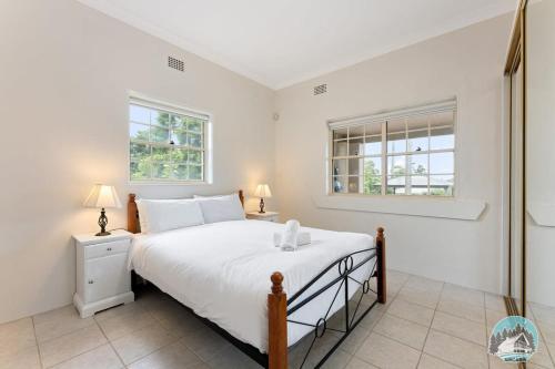 a white bedroom with a bed and two windows at Aircabin - Blakehurst - Spacious - 5 Beds House in Sydney