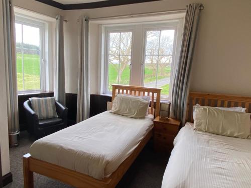 1 dormitorio con 2 camas, silla y ventanas en Kingarth Hotel en Kilchattan