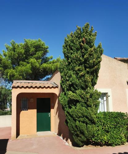 a building with a green door next to a tree at Résidence l'Oustal des Mers in Gruissan