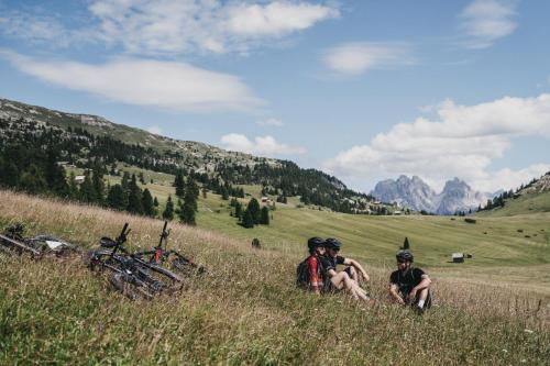 three people sitting in the grass in a field at Hotel Rudolf in Brunico