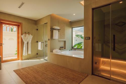 a bathroom with a tub and a glass shower at Naama Beach Villas & Spa in Al Aqah