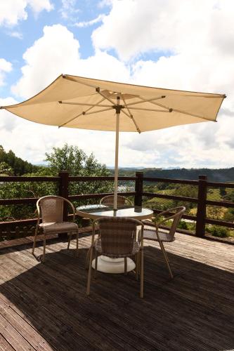 a table and chairs with an umbrella on a deck at Aldeia Flor de Liz - Pedra Azul in Pedra Azul
