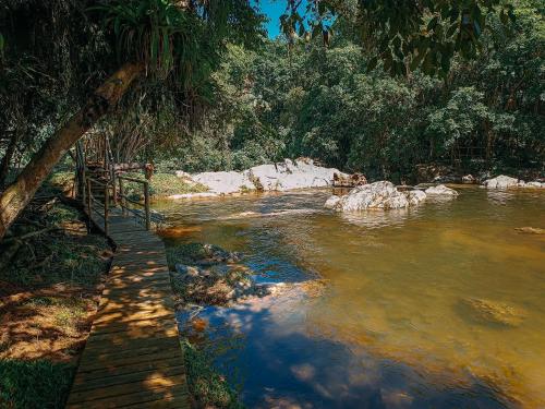 a river with a wooden walkway next to a forest at Suíte com cachoeira no quintal in Antônio Carlos