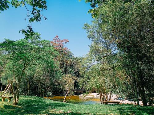 a view of a river with benches and trees at Suíte com cachoeira no quintal in Antônio Carlos