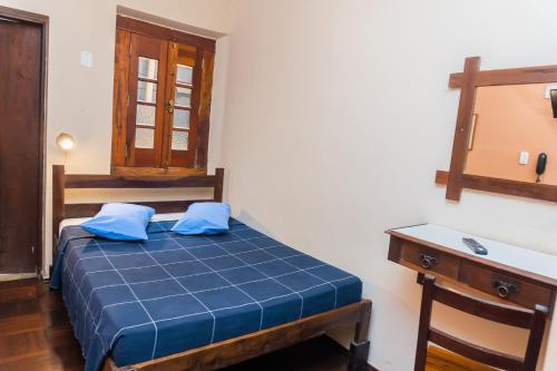 a bedroom with a bed with blue sheets and a desk at Hotel Colonial in São Lourenço