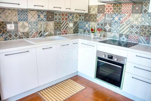 a kitchen with white cabinets and tiles on the wall at Aleari Villa Fanusa in Fanusa