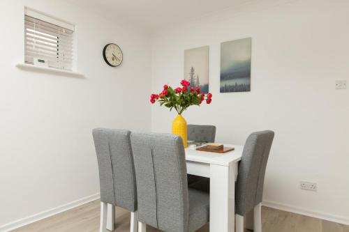 a dining room table with two chairs and a vase with red flowers at Stylish Seaside Stay – Brighton Marina Views in Brighton & Hove