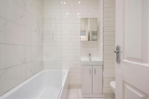 a white bathroom with a tub and a sink at Charming 1 Bedroom Flat with Private Patio - West London, Kensington, Earl's Court, Chelsea in London