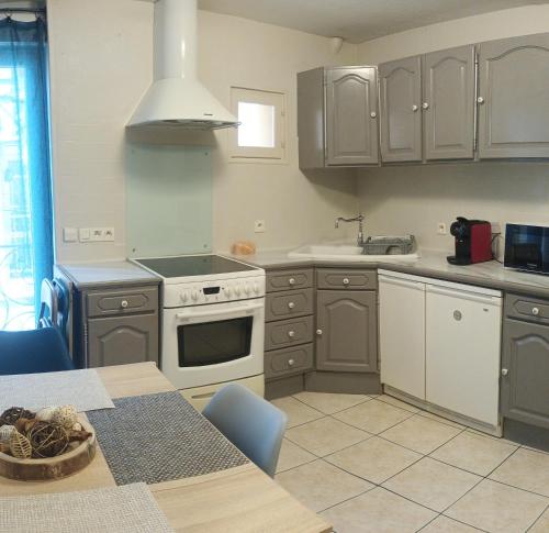 La cuisine est équipée de placards gris et d'une cuisinière blanche. dans l'établissement Maison coeur du village, à Sérignan