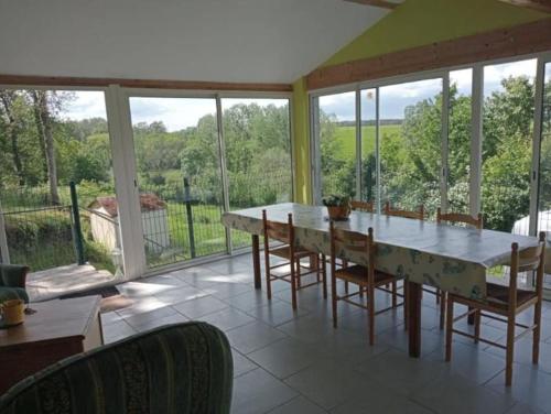 ein Esszimmer mit einem Tisch, Stühlen und Fenstern in der Unterkunft maison de campagne au calme, Le Lude in Le Lude