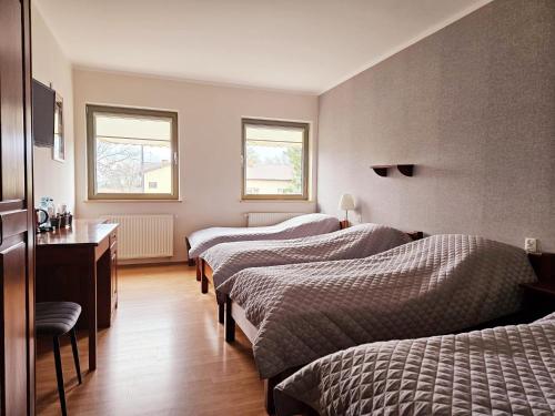 ルブリンにあるRestauracja Hotel Przystanのベッド3台、デスク、窓2つが備わる客室です。