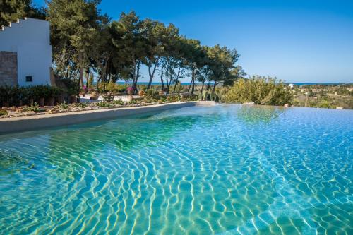 a swimming pool with blue water and trees at Hotel Masseria Fontanelle in Ugento
