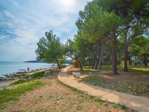 a path next to a beach with a bench and trees at Holiday Home Artatore by Interhome in Mali Lošinj