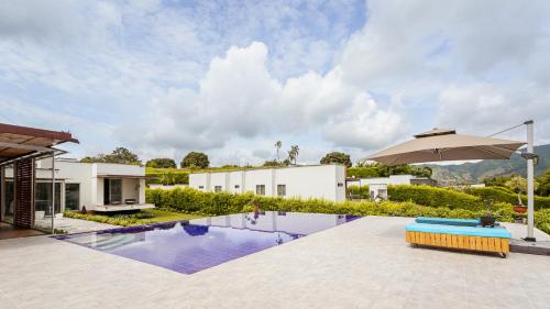 a swimming pool with an umbrella next to a house at Malugo Campestre in Pereira