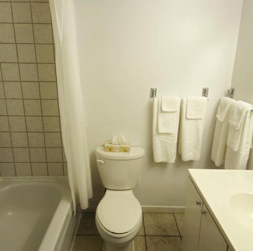a white bathroom with a toilet and a tub and towels at Motel Au Soleil couchant in Rimouski