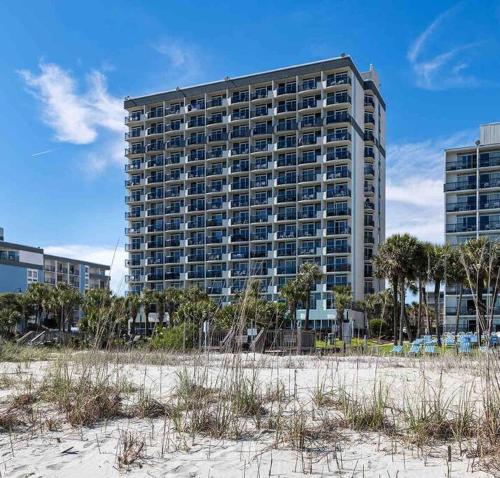 a tall building in front of a beach with trees at Tranquil Palms-Oceanfront Condo in Myrtle Beach