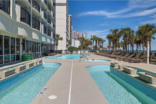 a resort swimming pool with chairs and a building at Tranquil Palms-Oceanfront Condo in Myrtle Beach