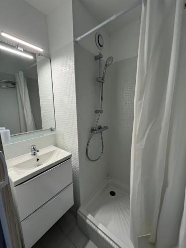 ein weißes Bad mit einer Dusche und einem Waschbecken in der Unterkunft Appartement 2 pièces + cabine, 6 couchages in Le Grau-du-Roi