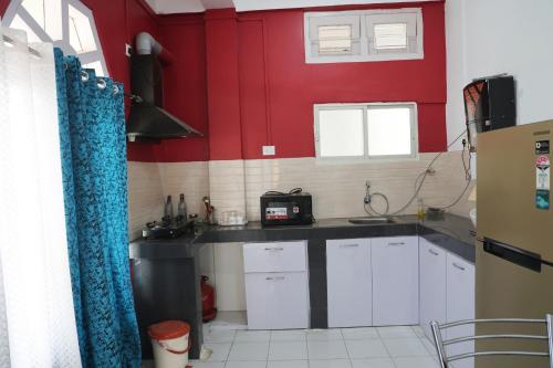 a small kitchen with red walls and white cabinets at Cozy Haven in Jorhāt