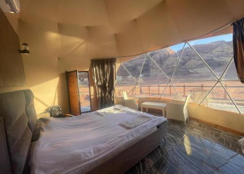 a bedroom with a bed and a large window at Desert Flower Camp Wadi Rum in Wadi Rum