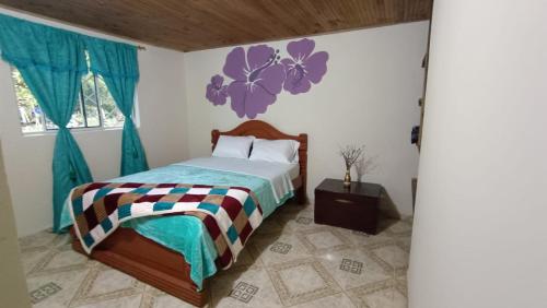 a bedroom with a bed with a purple flower on the wall at susurros del río in Pijao