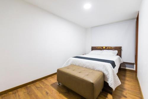 Habitación blanca con cama y reposapiés en Hotel Casa Botero 203, en Bogotá