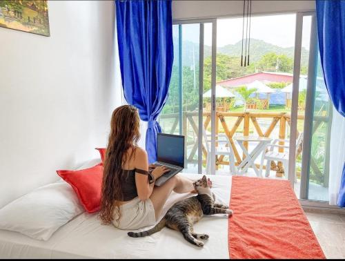 a woman sitting on a bed with a laptop and a cat at La Rivera Playa Palomino in Palomino