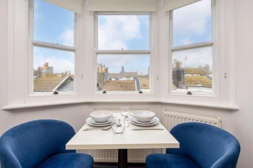 a table with two blue chairs and two windows at Cool & Chic Top Floor Studio Flat in Brighton & Hove