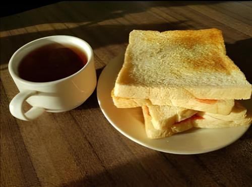 a plate with a sandwich and a cup of coffee at Tapian Asri Camp in Bukittinggi