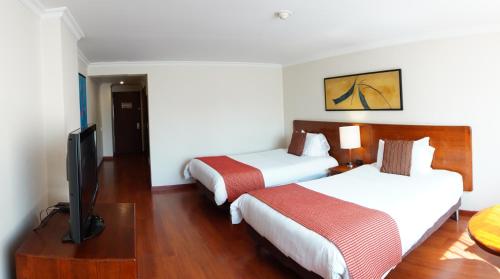a hotel room with two beds and a flat screen tv at HOTEL ILAR ESPERANZA CERCA DE EMBAJADA EEUU Y CORFERIAS in Bogotá