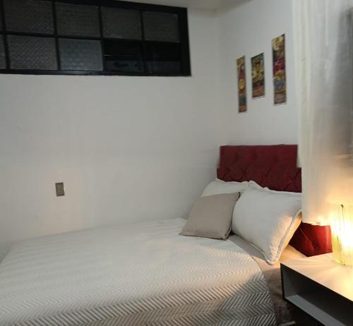 a white bedroom with a bed with a red headboard at Casa Qura Qura in Cochabamba
