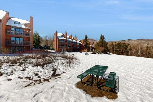 a green bench in the snow in front of a building at White Birch at Nordic Village in Bartlett