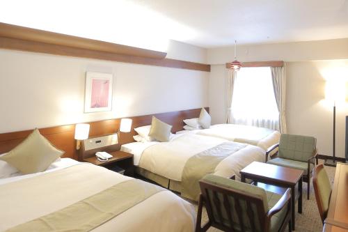 una camera d'albergo con tre letti, un tavolo e una sedia di Kurashiki Kokusai Hotel a Kurashiki