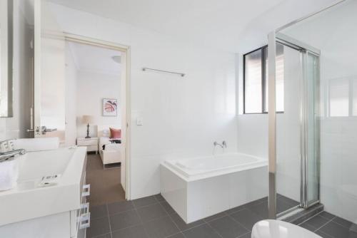 a white bathroom with a tub and a sink at Spacious Two-Bedroom Apartment near Hospital in Sydney
