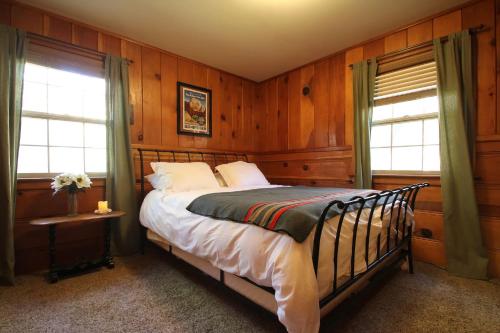 a bedroom with a bed with wooden walls and windows at Ahwahnee-be Vintage Cabin - Walk to town! in Idyllwild
