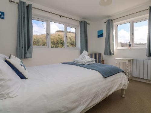 a bedroom with a large white bed with two windows at Cockle Island Cott in Porthallow