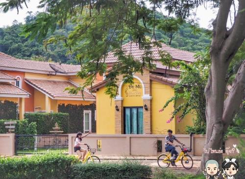 dos personas montando bicicletas en frente de un edificio amarillo en Demu Plus Pool villa @Marino Khaoyai, en Nong Nam Daeng