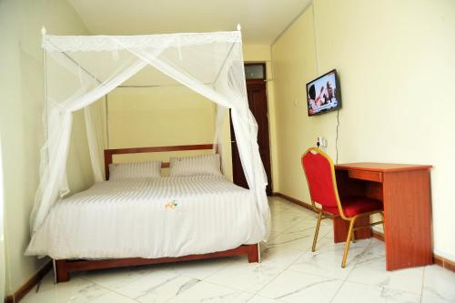 een slaapkamer met een hemelbed en een bureau bij Apollo Inn Fortportal in Kigarama