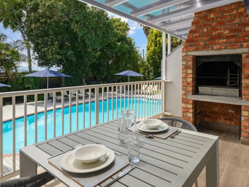 a table with plates and glasses on a patio with a pool at Formosa Bay in Plettenberg Bay