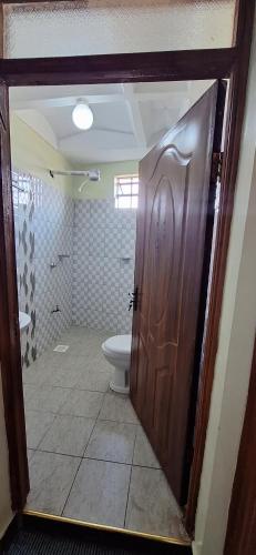 a bathroom with a toilet and a wooden door at Zedek Furnished Apartment 102 in Nairobi